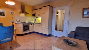 A compact kitchen with a stove, microwave, and cabinets, a dining area with a table and chairs, and a small seating area with a sofa. - Darss-Wieck, living room-kitchen-bedroom-balcony, sauna, 2- 3 persons, bicycle shed (Wieck)