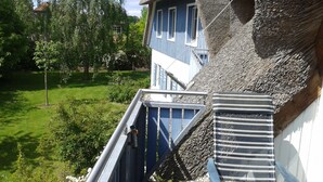 A building with a thatched roof and blue shutters, a metal staircase, and a view of a green garden. - Darss-Wieck, living room-kitchen-bedroom-balcony, sauna, 2- 3 persons, bicycle shed (Wieck)