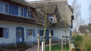 A traditional house with a thatched roof, blue shutters, and a narrow pathway leading to the entrance. - Darss-Wieck, living room-kitchen-bedroom-balcony, sauna, 2- 3 persons, bicycle shed (Wieck)
