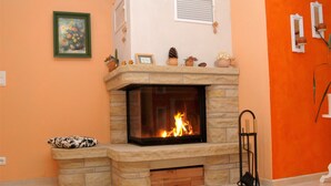 A stone fireplace with a visible fire, a framed picture on the wall, and a small shelf with decorative items. - Detached house, fireplace, huge garden, small stream, idyllic, tranquillity, pure nature (Mittenwalde)