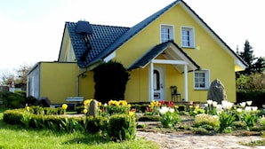 A yellow house with a sloped roof, a front porch, and a garden with tulips. - Detached house, fireplace, huge garden, small stream, idyllic, tranquillity, pure nature (Mittenwalde)