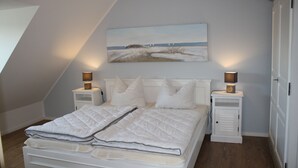 Un dormitorio con una cama, dos mesitas de noche con lámparas, un cuadro en la pared y una puerta.
