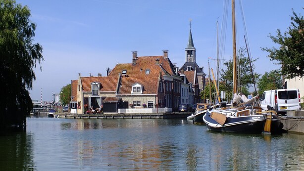 A canal with traditional buildings, a church tower, and boats docked. - Cozy "Schwedenhaus" with a beautiful view, located on the water (Idsegahuizum)