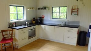 A compact kitchen with two windows, a sink, a kettle, and a stove. - Cozy "Schwedenhaus" with a beautiful view, located on the water (Idsegahuizum)