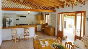 Une cuisine spacieuse avec des poutres en bois, un coin repas avec une table dressée pour quatre personnes, et une vue sur l’extérieur grâce à une porte vitrée.
