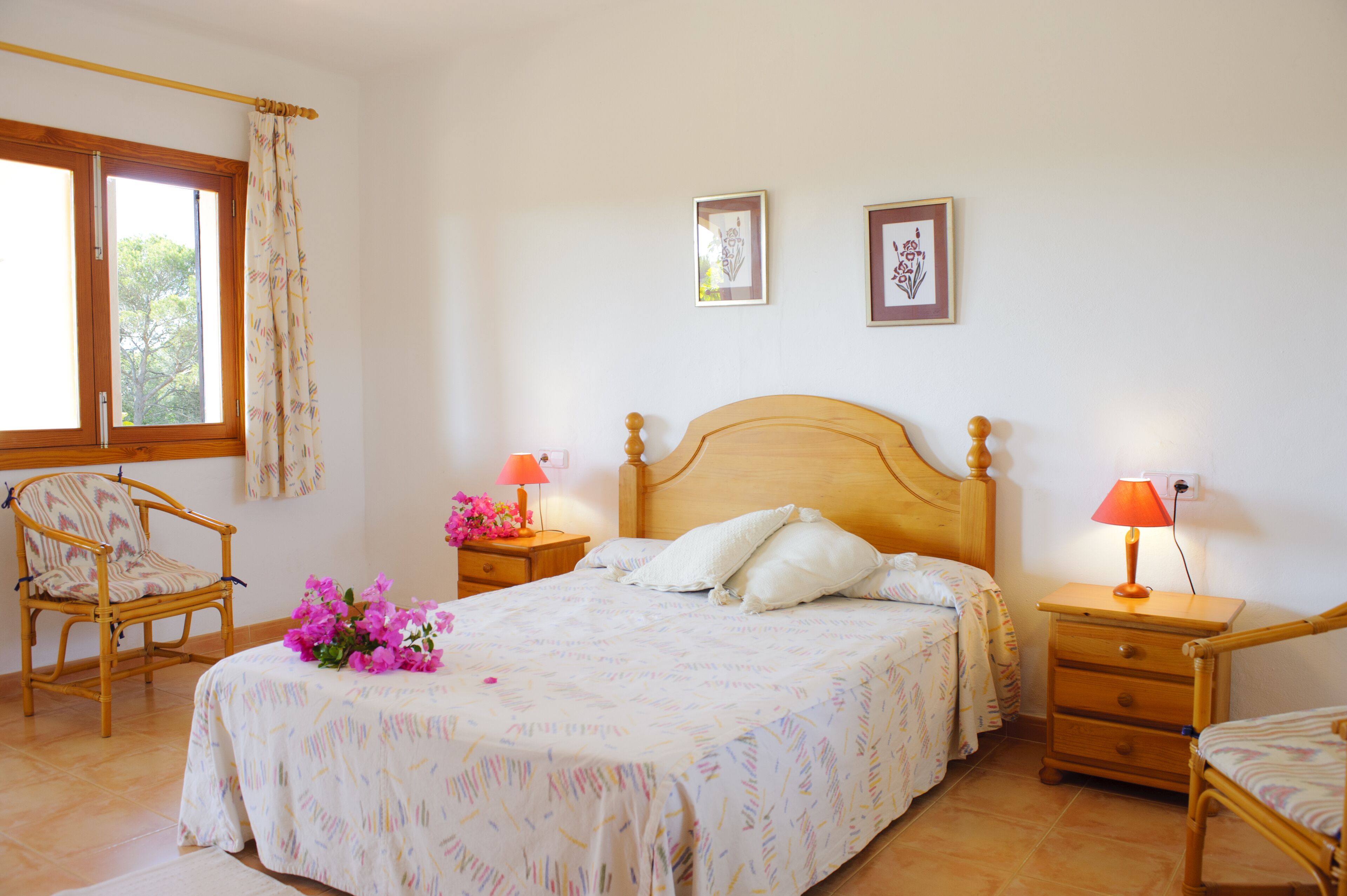 A bedroom with a large bed, two bedside tables with lamps, a chair, and a window with curtains.