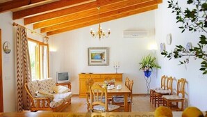 Une pièce chaleureuse avec un plafond en bois, un canapé, une table à manger avec des chaises, un téléviseur et une plante en pot.