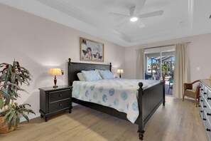 Une chambre à coucher avec un lit, des tables de chevet, un ventilateur de plafond, un tableau et une vue sur l’extérieur.