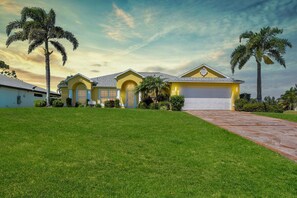 A residential house with a garage, a well-maintained lawn, and palm trees.
