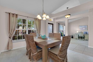 A dining area with a wooden table and wicker chairs, a chandelier, and a view of the outside.