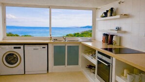 Een keuken met uitzicht op zee, voorzien van een wasmachine, vaatwasser en fornuis.