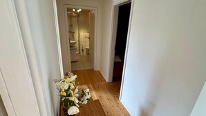 Un corridoio con pavimento in legno che conduce a un bagno con doccia e WC.