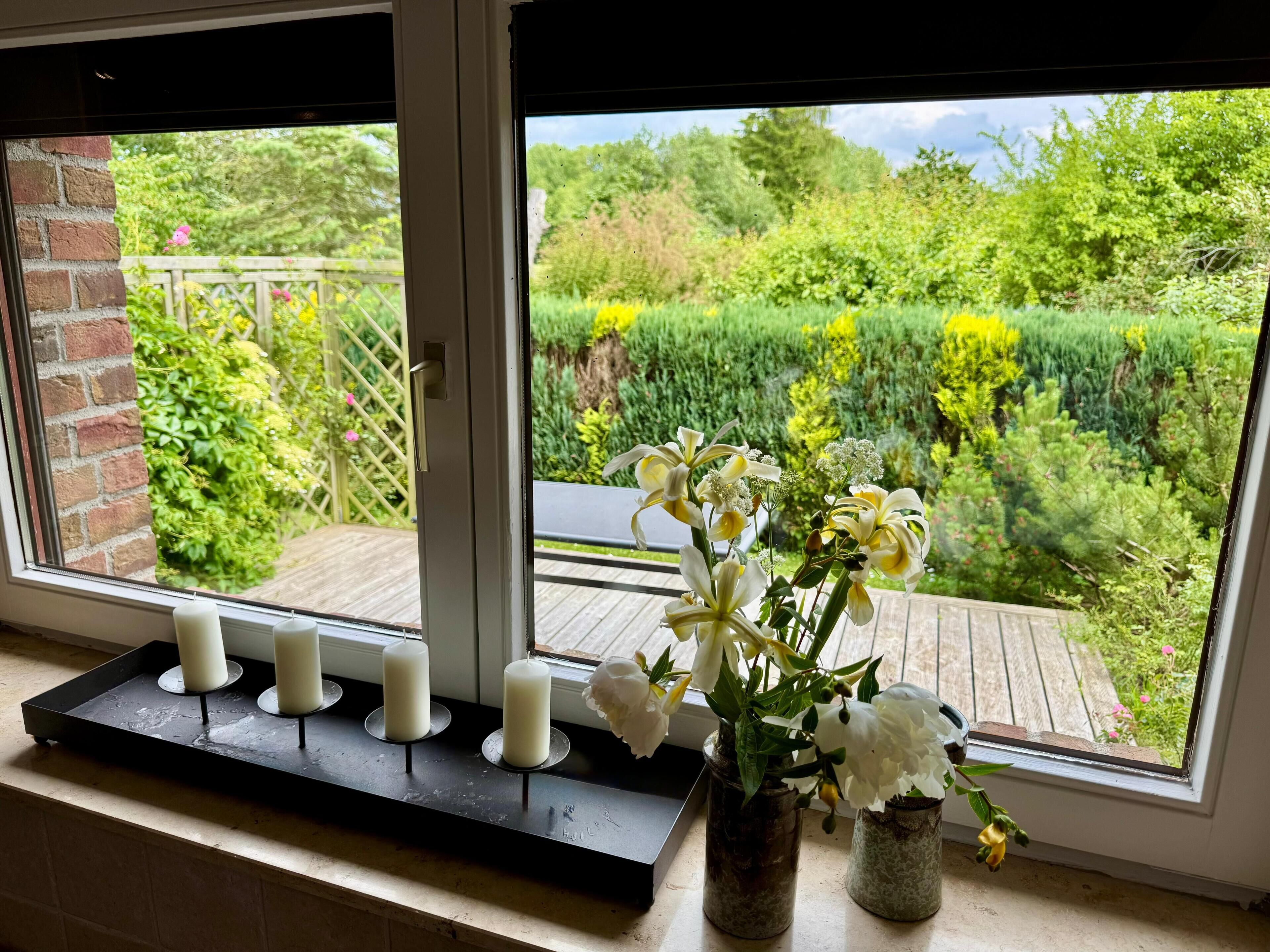 A window with a view of a garden, a candle holder with candles, and a vase with flowers.
