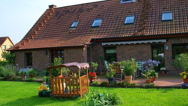 Una casa in mattoni con tetto in tegole, una casetta in legno e un giardino con piante in vaso.
