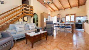 A spacious living area with a staircase, a sofa, a coffee table, and a kitchen in the background. - Finca Son Rebassa (Sant Joan)