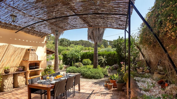 An outdoor patio with a table set for dining, surrounded by potted plants and a stone wall. - Finca Son Rebassa (Sant Joan)