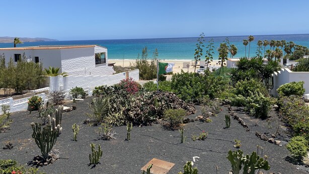 Vista costera con un edificio blanco, una playa arenosa y un cielo azul despejado.