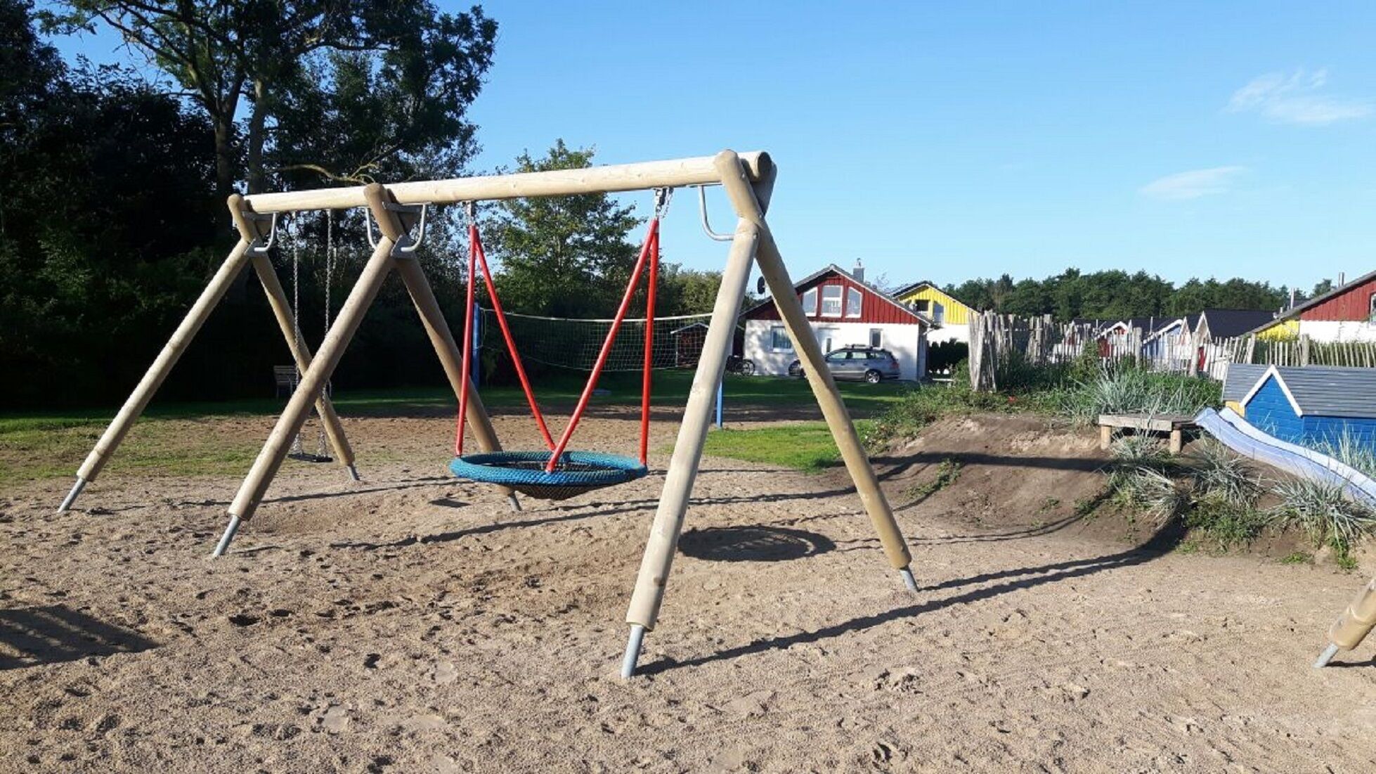 A swing set in a sandy area with a dirt path and wooden fences in the background.