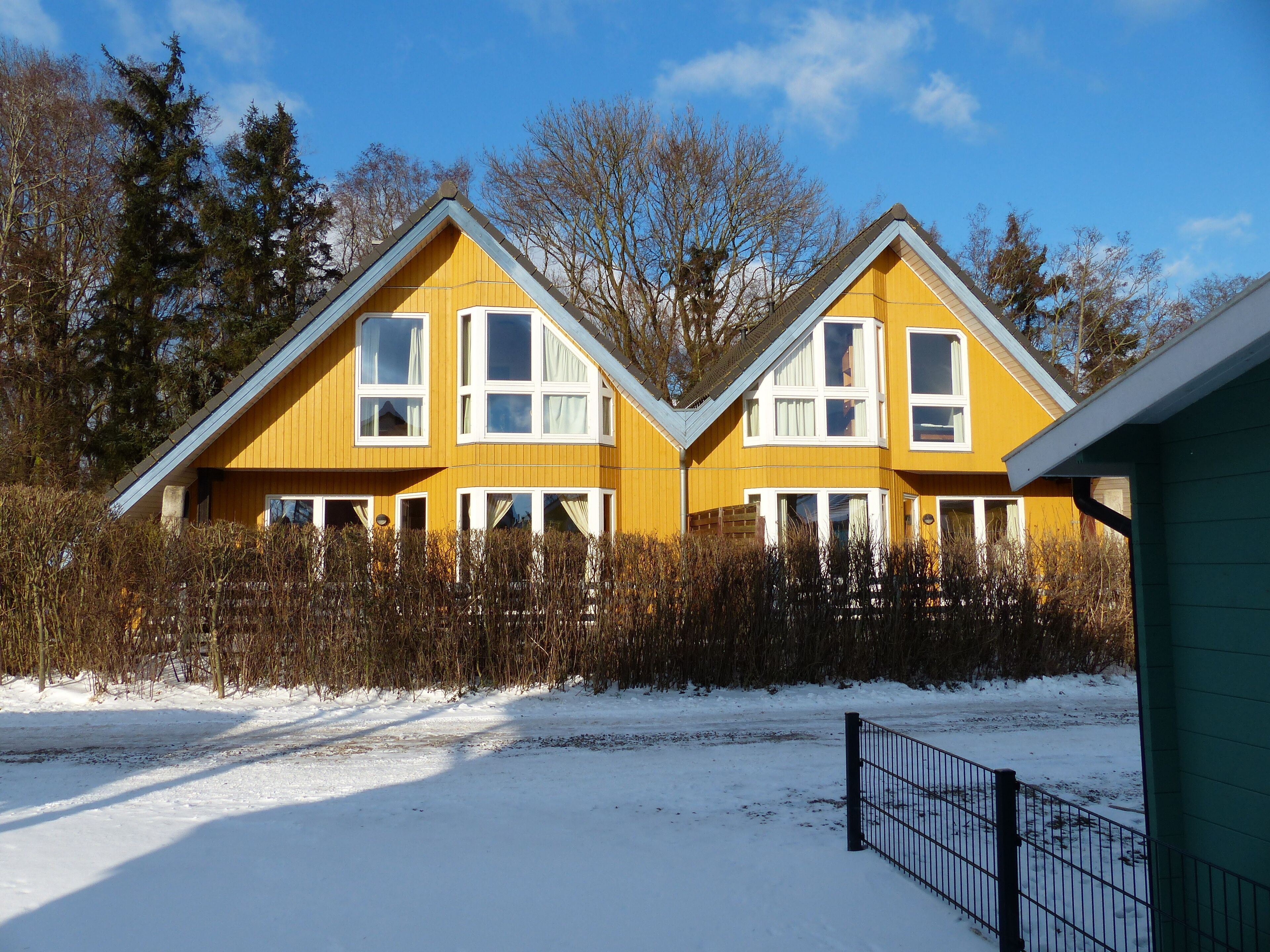 A yellow two-story house with multiple windows and a snow-covered ground.