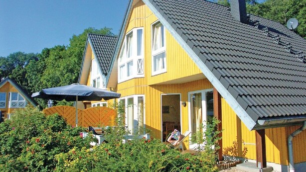Ein gelbes Haus mit grauem Dach, einer Satellitenschüssel und einem Garten mit Büschen und einem Stuhl.