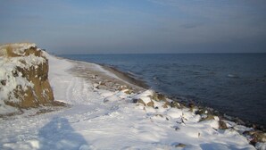 Ein verschneiter Strand mit felsigem Ufer und ruhiger See.