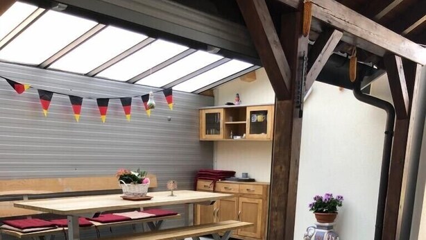 Een buitenpatio met een houten tafel en banken, een potplant en een uitzicht op de lucht door een dakraam.