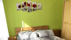 Een slaapkamer met een bed, nachtkastjes, een houten tafel en een stoel. Boven het bed hangen vier schilderijen aan de muur.