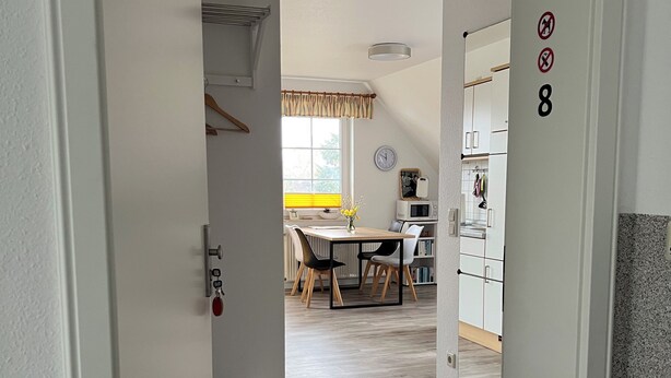 Un couloir mène à une salle à manger où se trouvent une table et des chaises, un four à micro-ondes et une horloge murale.