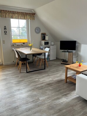 Una habitación moderna y luminosa con mesa de comedor, sillas, televisor y una pequeña cocina americana.
