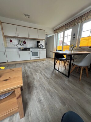 Una cocina moderna con armarios blancos, una mesa de comedor de madera y vistas al exterior a través de amplios ventanales.