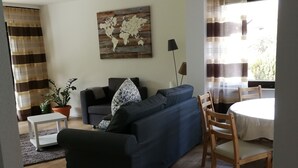 Una sala de estar con un sofá, una mesa de comedor con sillas, un cuadro con un mapa del mundo y una planta en maceta.