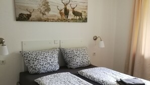 Una cama doble con ropa de cama estampada, un cabecero, dos lámparas de pared y un cuadro con motivos de ciervo sobre la cama.