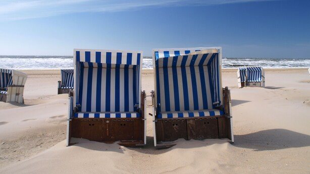 Strandstole med blåt og hvidt stribemønster på en sandstrand.