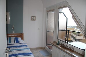 A bedroom with a bed, a window with a view, a radiator, and a bedside table.