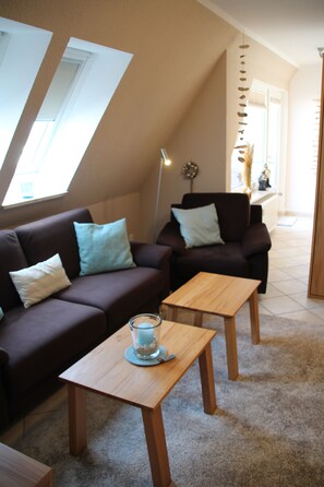 A modern living room with a brown sofa, two wooden side tables, and a glass candle holder.