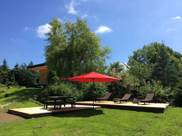 Un espacio al aire libre con un porche de madera, un paraguas rojo y varias sillas de lounge.