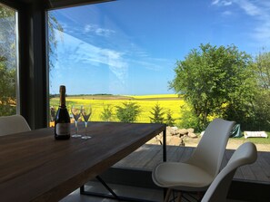 A dining table with a bottle and glasses, a chair, and a view of a yellow field through large windows. - "Finca Baltica": Baltic Sea dream vacation on 3500 sqm with an exclusive sauna house (Wichmannsdorf)