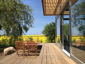 Una terraza al aire libre con mobiliario de madera, un pérgola y vistas a un campo amarillo.