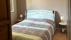A bed with a floral-patterned bedspread, two bedside tables with lamps, and a wooden door. - the gites les chênes n. 2, private pool and spa (Servas Gard)