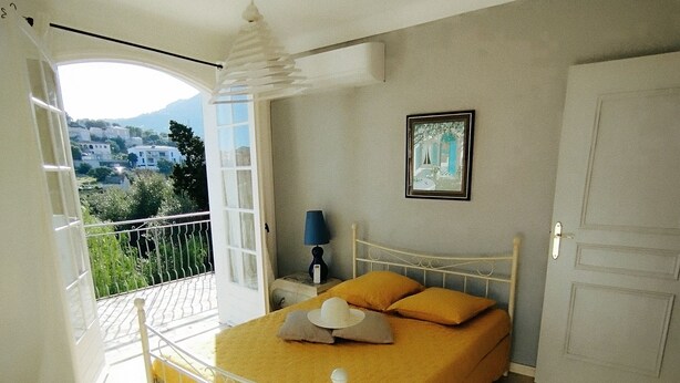 A bedroom with a bed, a nightstand, a lamp, a framed picture, and a view of the outside.