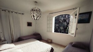 A bedroom with a large bed, a smaller bed, a window with a view of trees, a hanging light fixture, and a small table with a chair.