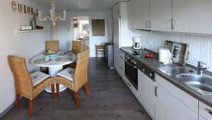 Una cucina compatta con zona pranzo, che include un tavolo rotondo, sedie in vimini, forno a incasso e macchina da caffè.