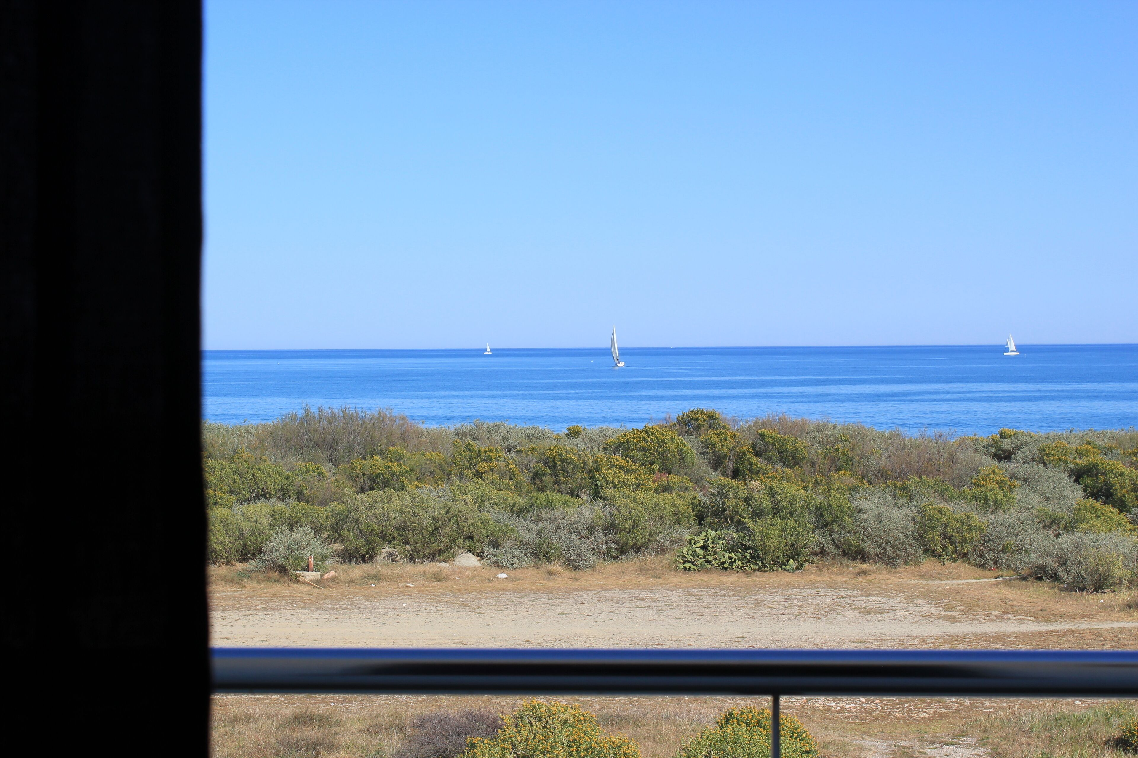 A coastal landscape with a clear view of the sea and distant sailboats.