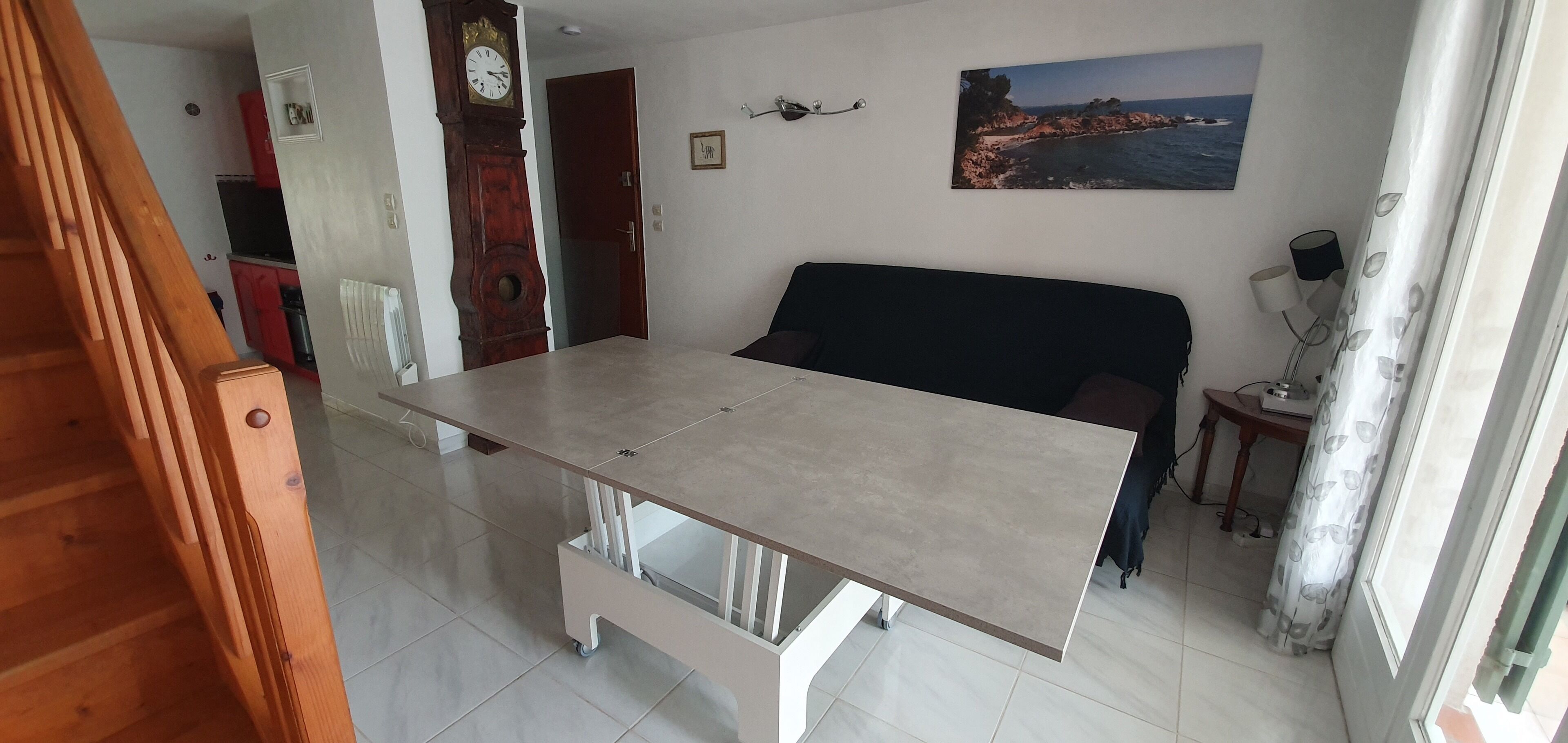 Een eethoek met een tafel, stoelen, een klok en een schilderij aan de muur.