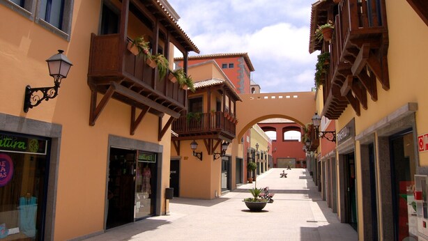 A narrow street with buildings featuring balconies and shop fronts. - Cozy apartment in a well-kept complex with pool, only 40 meters to the beach (Corralejo)