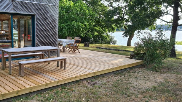 A wooden deck with a table and chairs, a bench, and a view of a lake. - WOODEN HOUSE ON THE GULF OF MORBIHAN (Crach)
