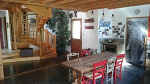 A wooden staircase leading to a loft, a dining area with a wooden table and red chairs, and a kitchen area with a refrigerator and a large elephant decoration. - WOODEN HOUSE ON THE GULF OF MORBIHAN (Crach)