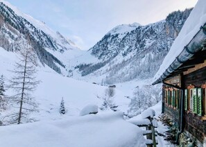 Een besneeuwd berglandschap met een houten chalet met traditionele architectuur en uitzicht over een vallei.