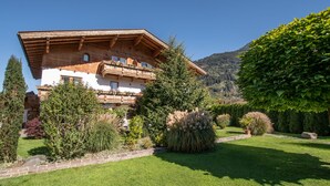 Eine traditionelle Chalet mit Holzbalkon, umgeben von gepflegten Gärten und einer Bergkulisse.