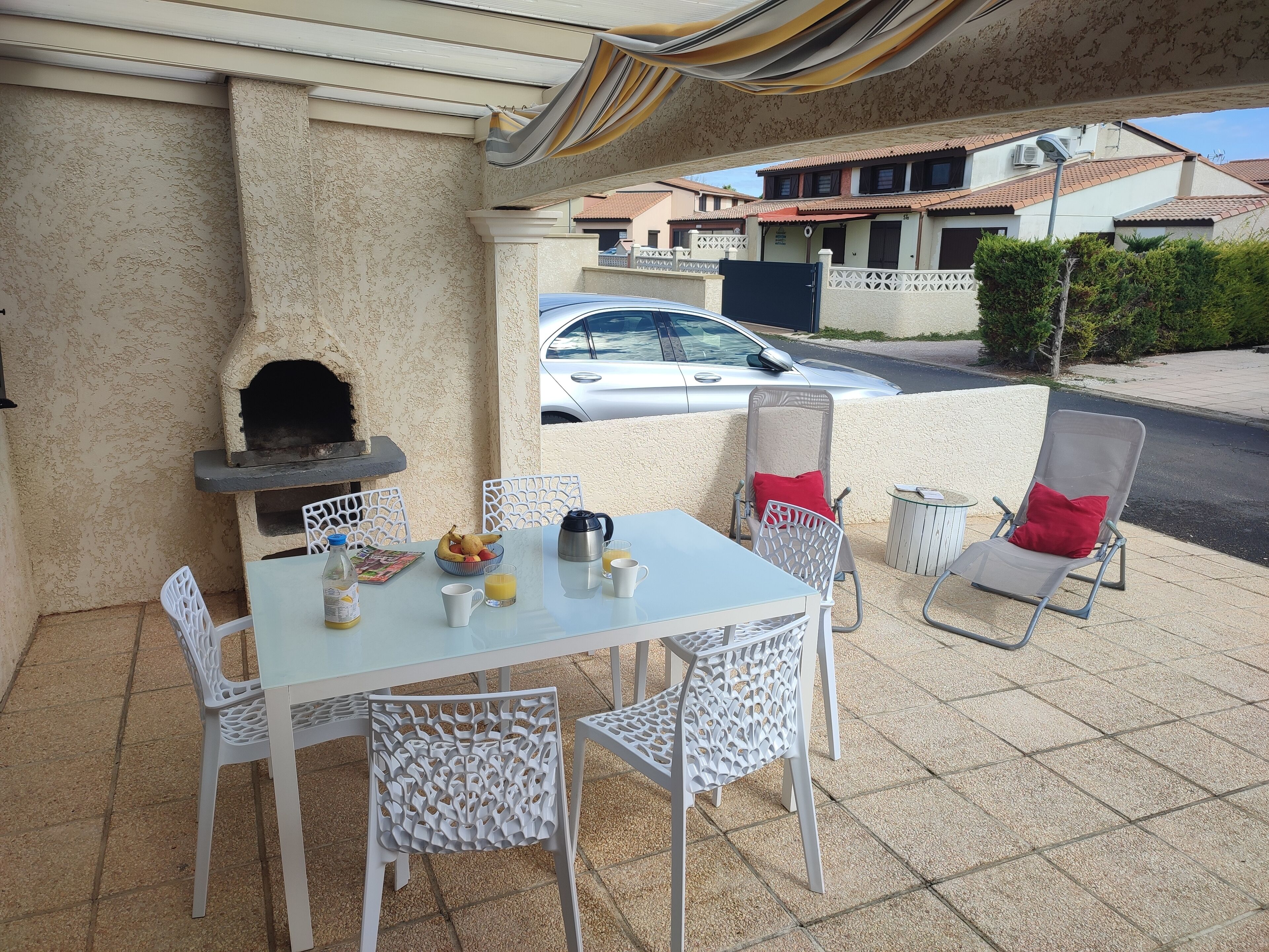 Un patio al aire libre con una mesa, sillas, una parrilla y un automóvil estacionado al fondo.